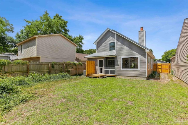 rear view of property with a fenced backyard, a yard, a chimney, and a sunroom