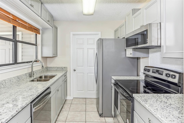 kitchen with a textured ceiling, light stone counters, a sink, light tile patterned floors, and stainless steel appliances