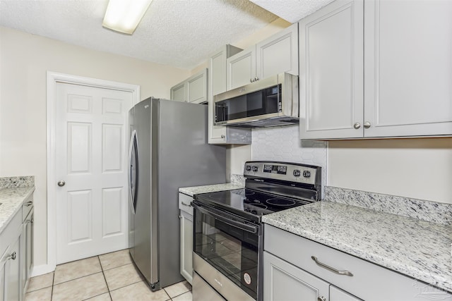 kitchen with a textured ceiling, light tile patterned floors, light stone countertops, and stainless steel appliances