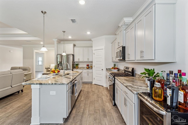 kitchen featuring appliances with stainless steel finishes, light wood-type flooring, decorative light fixtures, a center island with sink, and white cabinetry