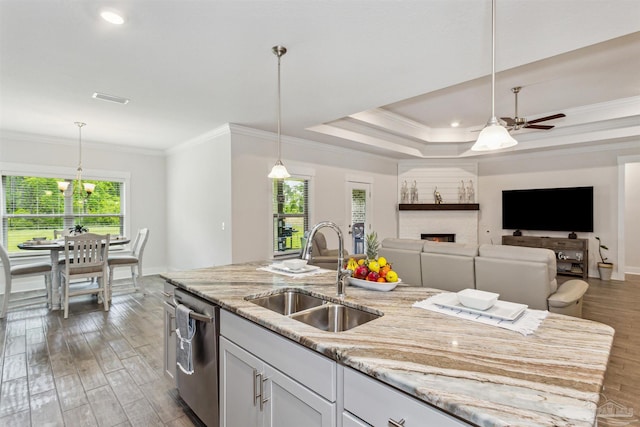 kitchen featuring dishwasher, sink, light stone counters, and a center island with sink