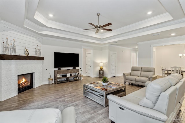 living room featuring a raised ceiling, a fireplace, ceiling fan, and crown molding