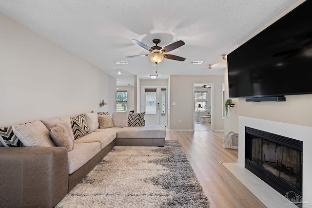 living area featuring a fireplace with flush hearth, visible vents, light wood-style flooring, and a textured ceiling