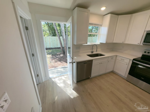 kitchen with light wood-type flooring, white cabinetry, appliances with stainless steel finishes, and a sink