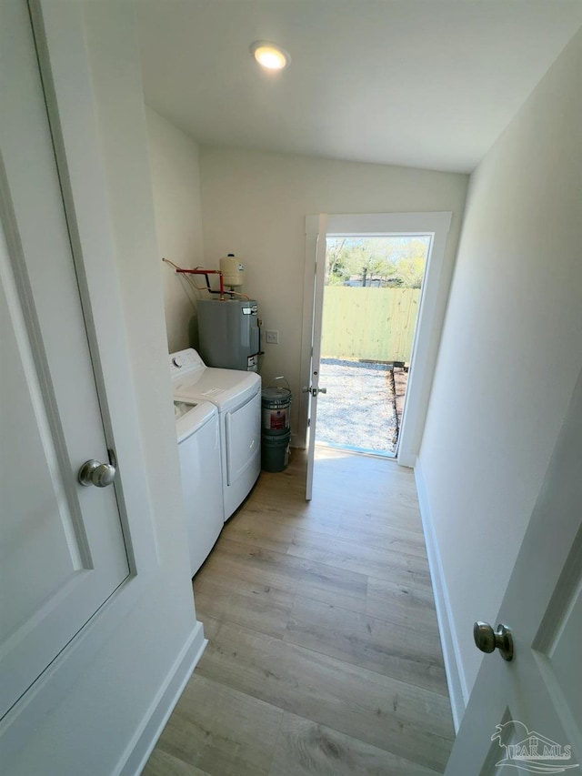 clothes washing area with washing machine and clothes dryer, water heater, light wood-type flooring, laundry area, and baseboards