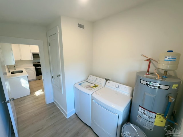 clothes washing area featuring water heater, visible vents, light wood-style floors, washer and dryer, and laundry area