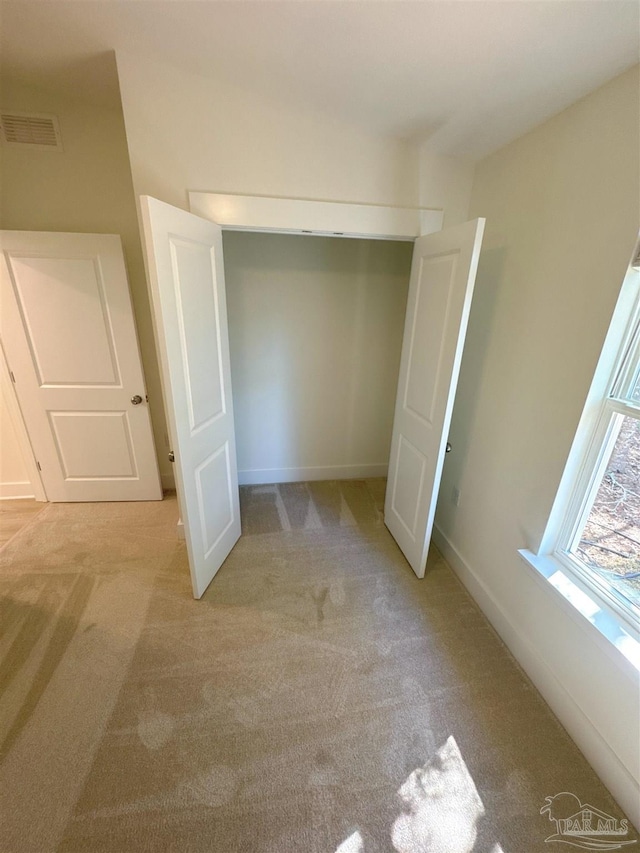 unfurnished bedroom featuring a closet, light carpet, visible vents, and baseboards