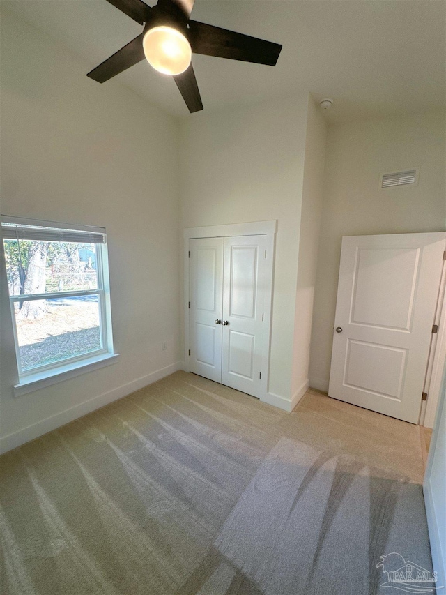 unfurnished bedroom with baseboards, visible vents, ceiling fan, carpet, and a high ceiling