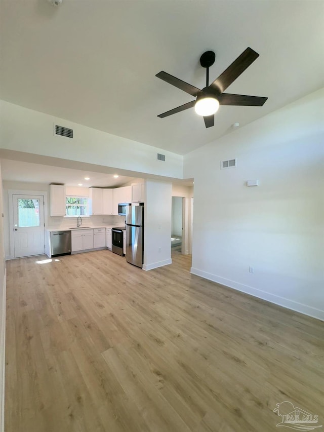 unfurnished living room with lofted ceiling, visible vents, a sink, and light wood finished floors