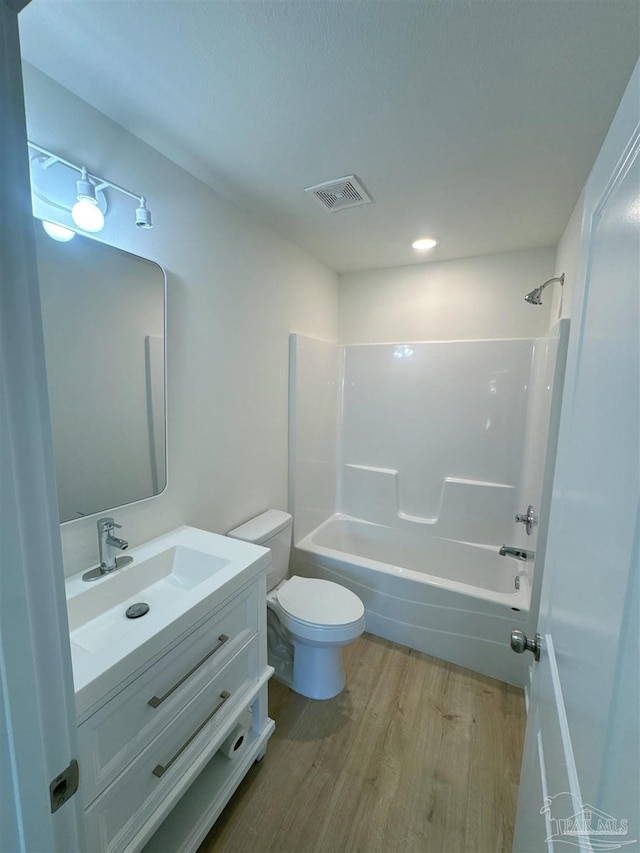 bathroom with visible vents, toilet, shower / bathtub combination, wood finished floors, and vanity