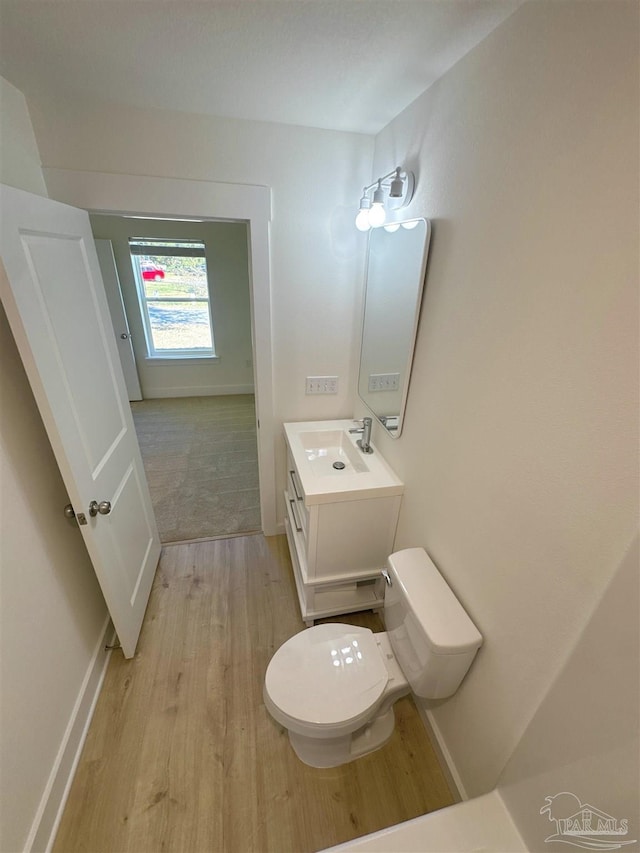 half bathroom featuring toilet, baseboards, wood finished floors, and vanity