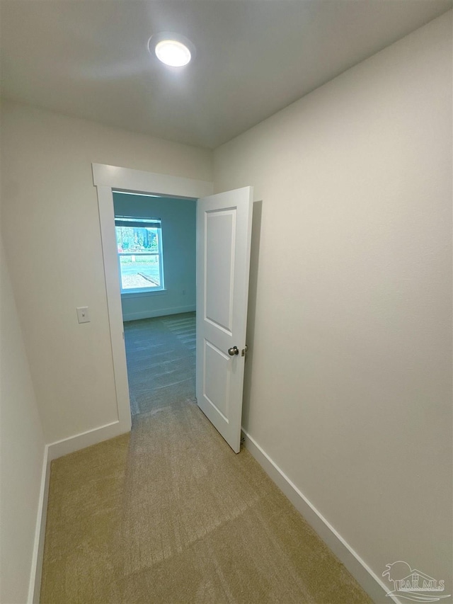 hallway with baseboards and light colored carpet