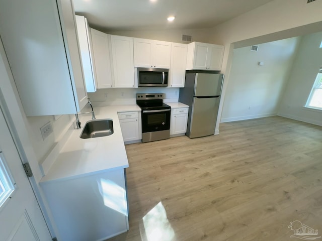 kitchen with appliances with stainless steel finishes, vaulted ceiling, white cabinets, and a sink