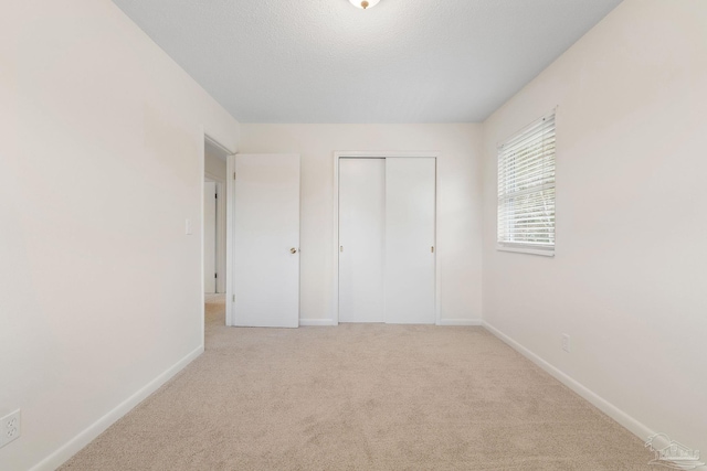 unfurnished bedroom featuring a textured ceiling, light colored carpet, and a closet