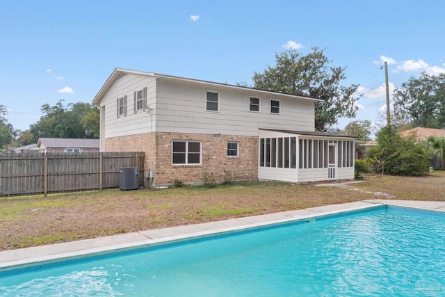 back of property with central air condition unit, a sunroom, a yard, and a fenced in pool