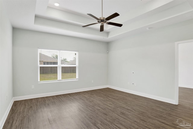 unfurnished room featuring a ceiling fan, a tray ceiling, dark wood-style floors, and baseboards