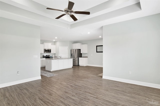 unfurnished living room with recessed lighting, baseboards, a ceiling fan, dark wood-type flooring, and a tray ceiling