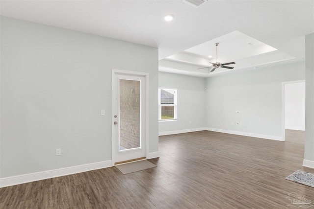 unfurnished living room with wood finished floors, a raised ceiling, a ceiling fan, and baseboards