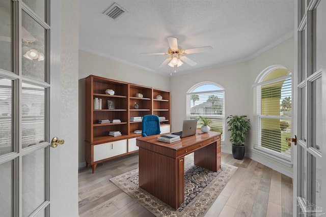 office with visible vents, crown molding, light wood-style flooring, a textured ceiling, and a ceiling fan