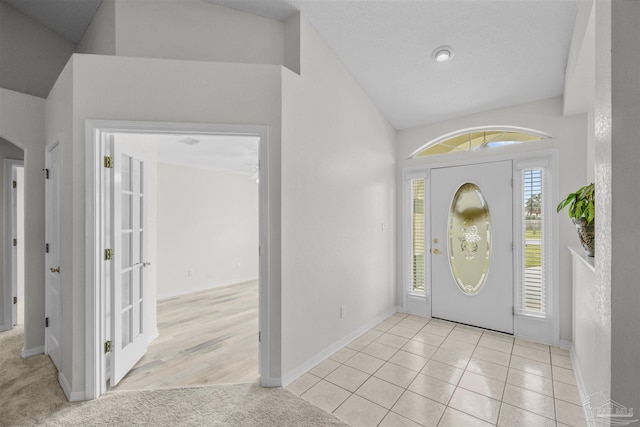 carpeted entrance foyer with tile patterned floors, baseboards, and vaulted ceiling