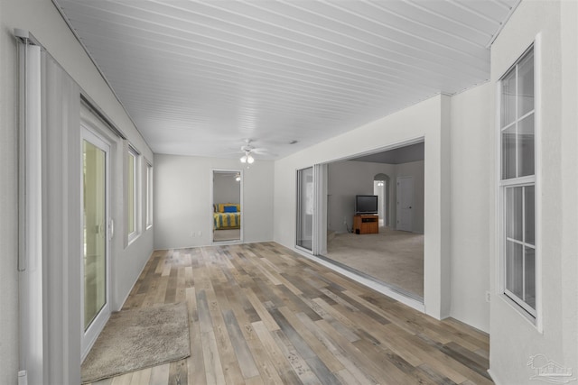 interior space featuring arched walkways, light wood-style floors, and a ceiling fan