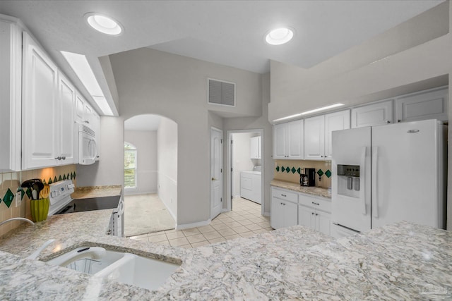 kitchen featuring visible vents, light stone counters, arched walkways, white appliances, and white cabinetry