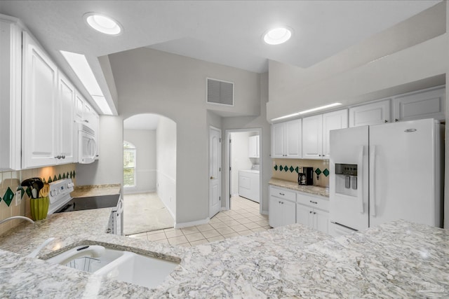 kitchen with white appliances, light stone countertops, visible vents, arched walkways, and white cabinets