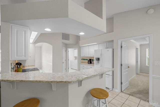 kitchen with light stone counters, white refrigerator with ice dispenser, a breakfast bar area, white cabinets, and washer / dryer