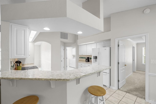 kitchen featuring light stone counters, white refrigerator with ice dispenser, white cabinetry, a breakfast bar area, and washer / dryer