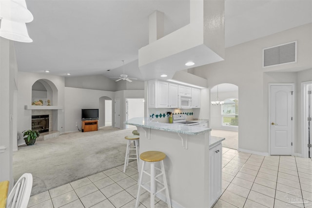 kitchen with visible vents, a tiled fireplace, white appliances, arched walkways, and light colored carpet