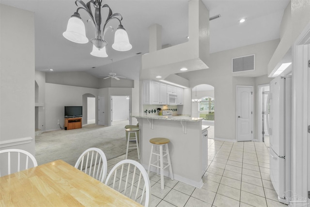 kitchen with white appliances, light tile patterned floors, visible vents, arched walkways, and light carpet