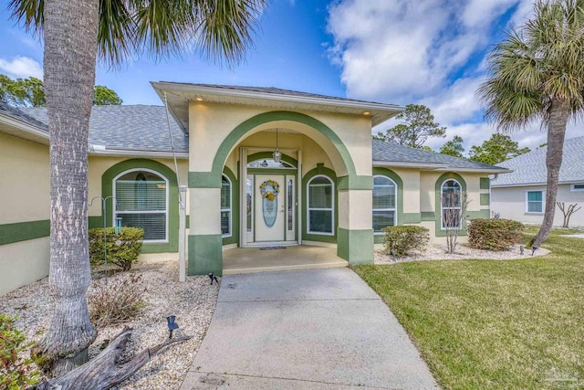 doorway to property featuring stucco siding, a lawn, and a shingled roof