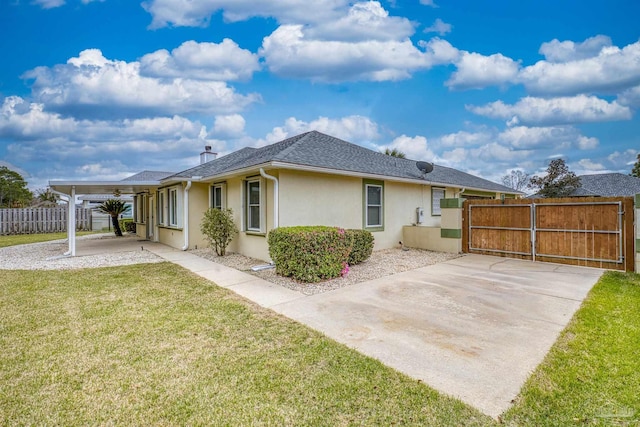 back of property featuring a shingled roof, fence, stucco siding, a lawn, and a gate