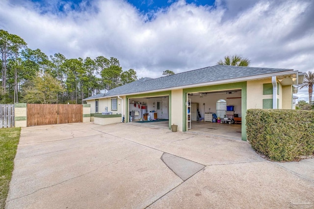 back of house with stucco siding, concrete driveway, fence, and a shingled roof