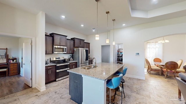 kitchen with light stone countertops, sink, decorative light fixtures, a kitchen island with sink, and appliances with stainless steel finishes