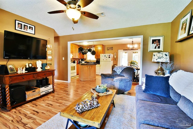 living room with ceiling fan with notable chandelier, light wood-type flooring, sink, and a textured ceiling