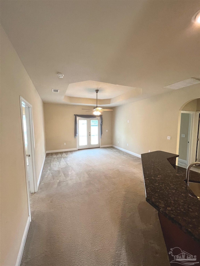 3026 Windward Cove Ct, Gulf Breeze, FL 32563 - unfurnished living room featuring a tray ceiling, arched walkways, light colored carpet, and a ceiling fan