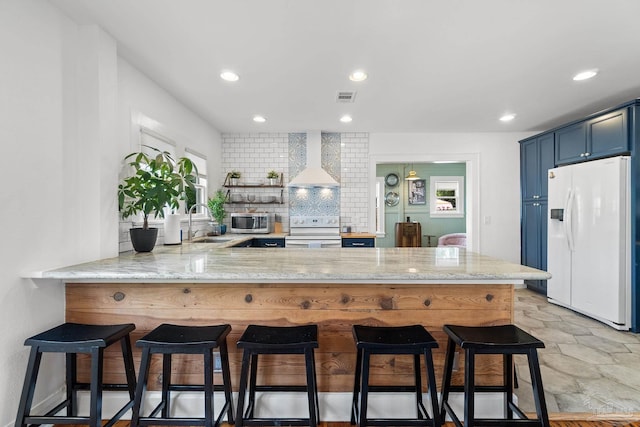 kitchen with wall chimney range hood, white appliances, sink, blue cabinets, and kitchen peninsula