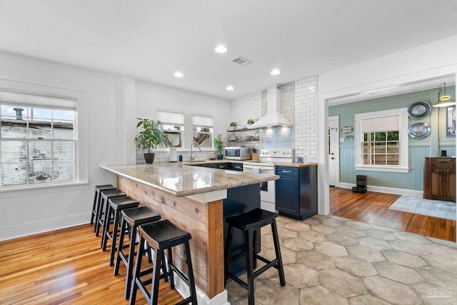 kitchen featuring light hardwood / wood-style floors, kitchen peninsula, a kitchen bar, a wealth of natural light, and range with electric cooktop