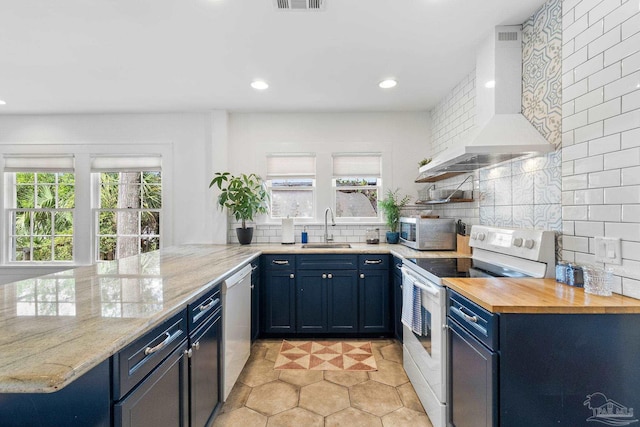 kitchen with kitchen peninsula, wall chimney exhaust hood, sink, blue cabinetry, and electric range oven