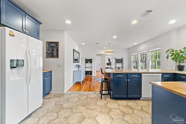 kitchen featuring hanging light fixtures, blue cabinetry, a kitchen breakfast bar, wood counters, and white appliances