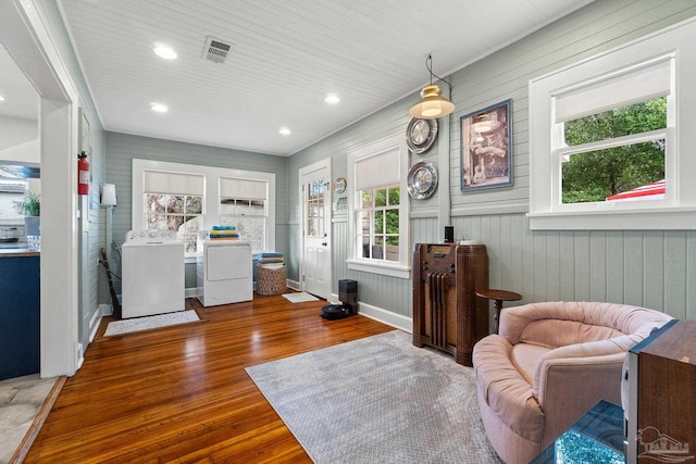 living area featuring dark hardwood / wood-style flooring, wood walls, independent washer and dryer, and plenty of natural light