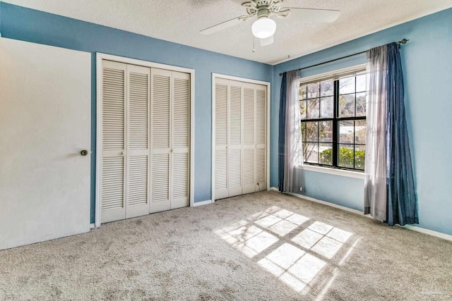 unfurnished bedroom featuring ceiling fan, light colored carpet, a textured ceiling, and two closets