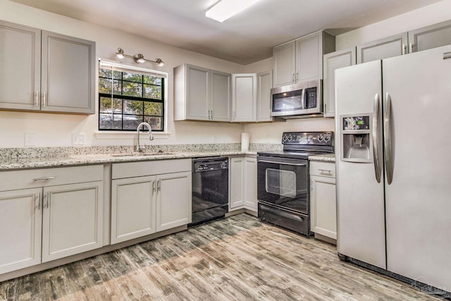 kitchen featuring sink, light stone counters, light hardwood / wood-style flooring, gray cabinets, and black appliances