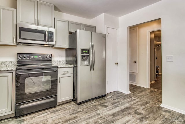 kitchen with light stone countertops, stainless steel appliances, gray cabinets, and wood-type flooring