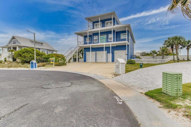 beach home with stairway, fence, a balcony, a garage, and driveway