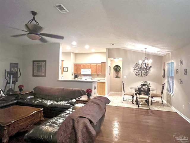 living area featuring lofted ceiling, light wood-type flooring, baseboards, ceiling fan with notable chandelier, and visible vents