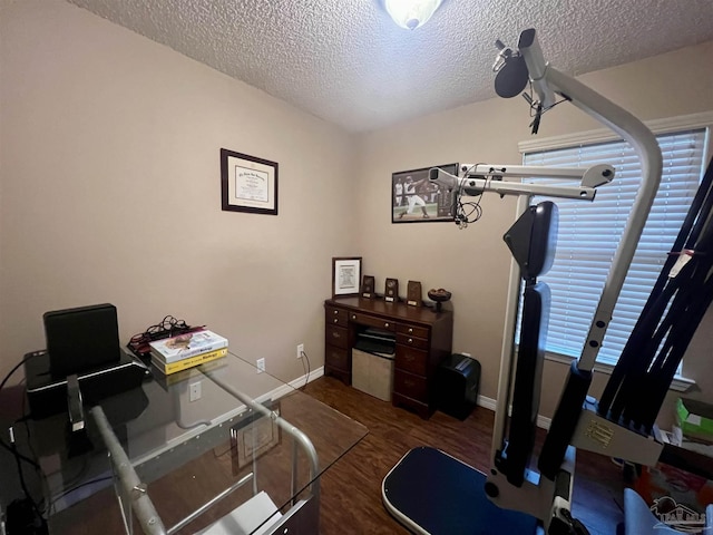 exercise area featuring baseboards, wood finished floors, and a textured ceiling