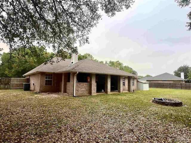 back of property with an outdoor structure, a fenced backyard, a storage unit, a fire pit, and central AC