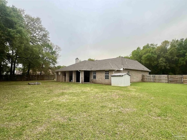 back of house with a chimney, an outbuilding, a fenced backyard, a storage unit, and a lawn